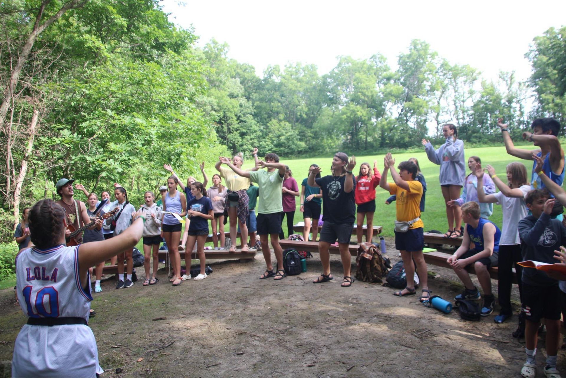 Group of hikers stretching and dancing in a forest clearing, with trees and dirt ground all around