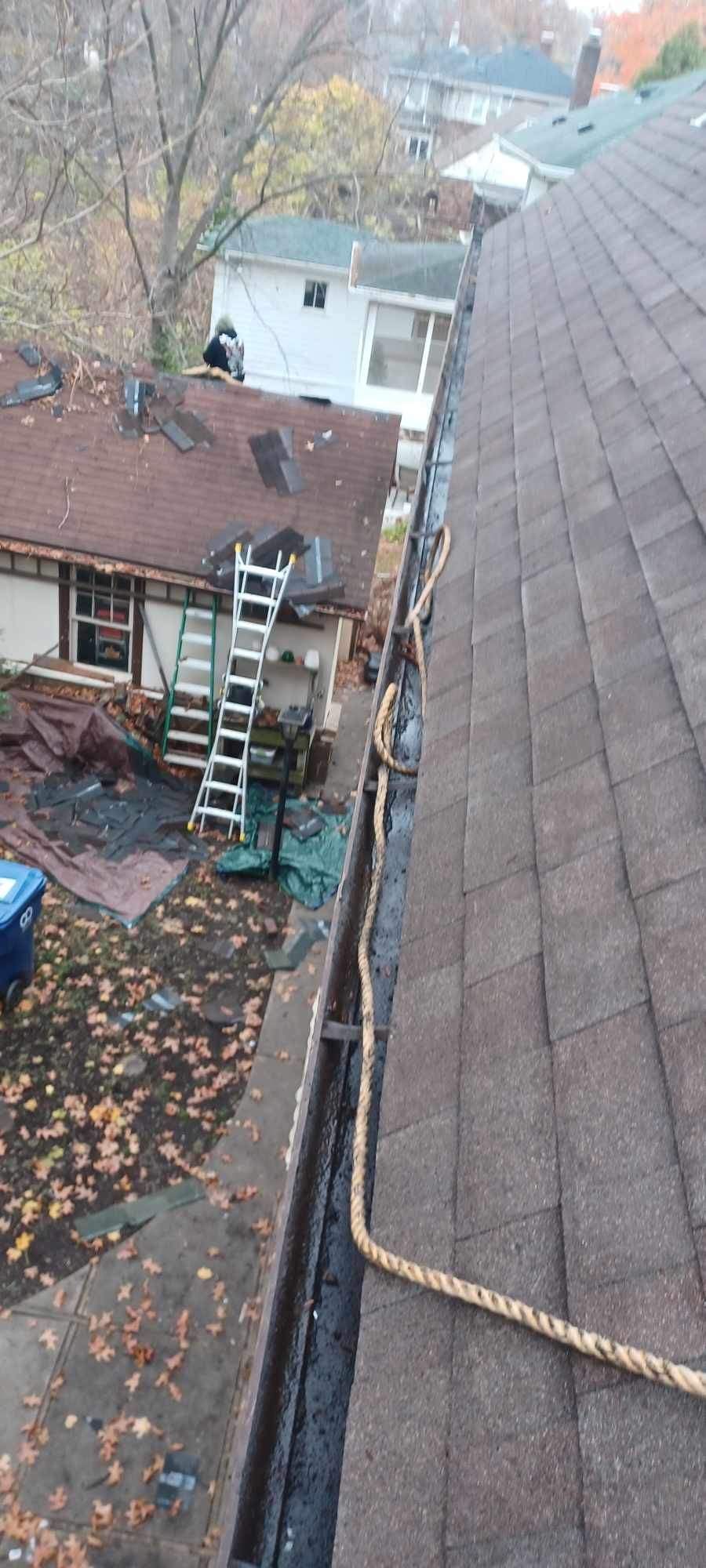 Rainy backyard with roof and ladders, leaves on the ground, and neighboring houses beyond.
