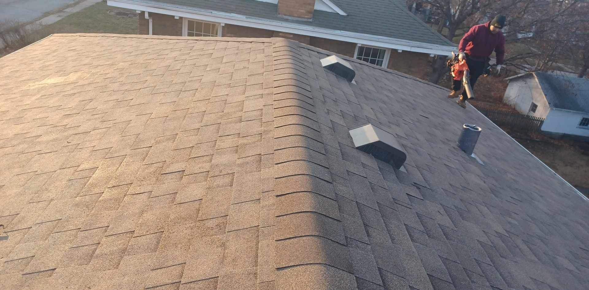 Two roofers on a shingled roof installing materials near the ridge at sunset.