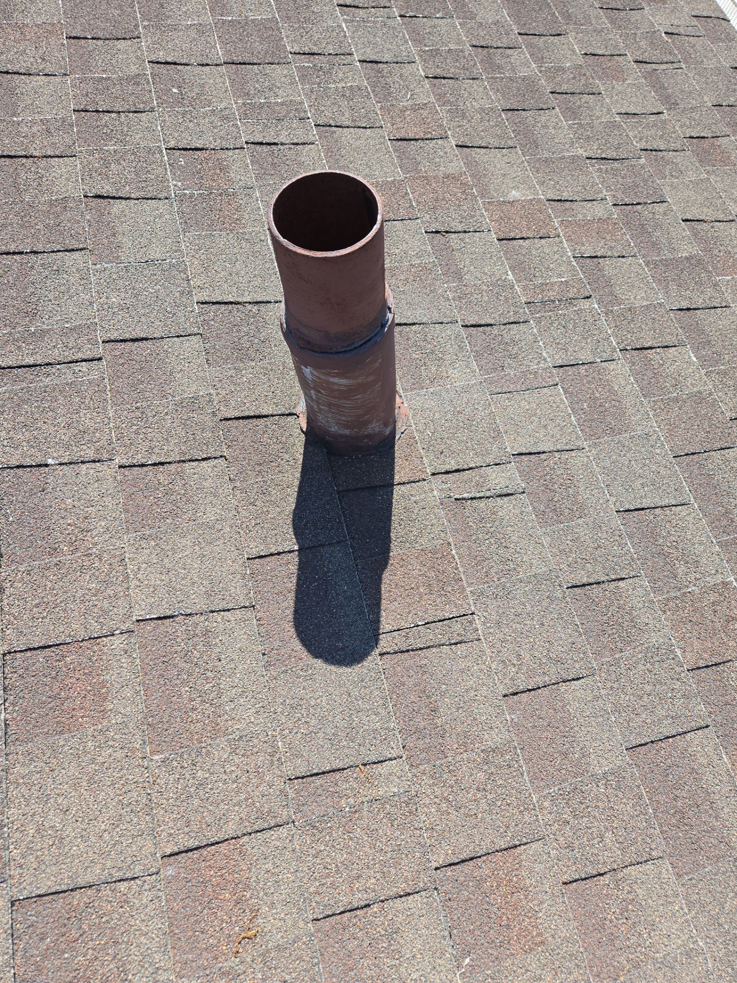 Rust-colored chimney pipe on a shingled roof, casting a long shadow.