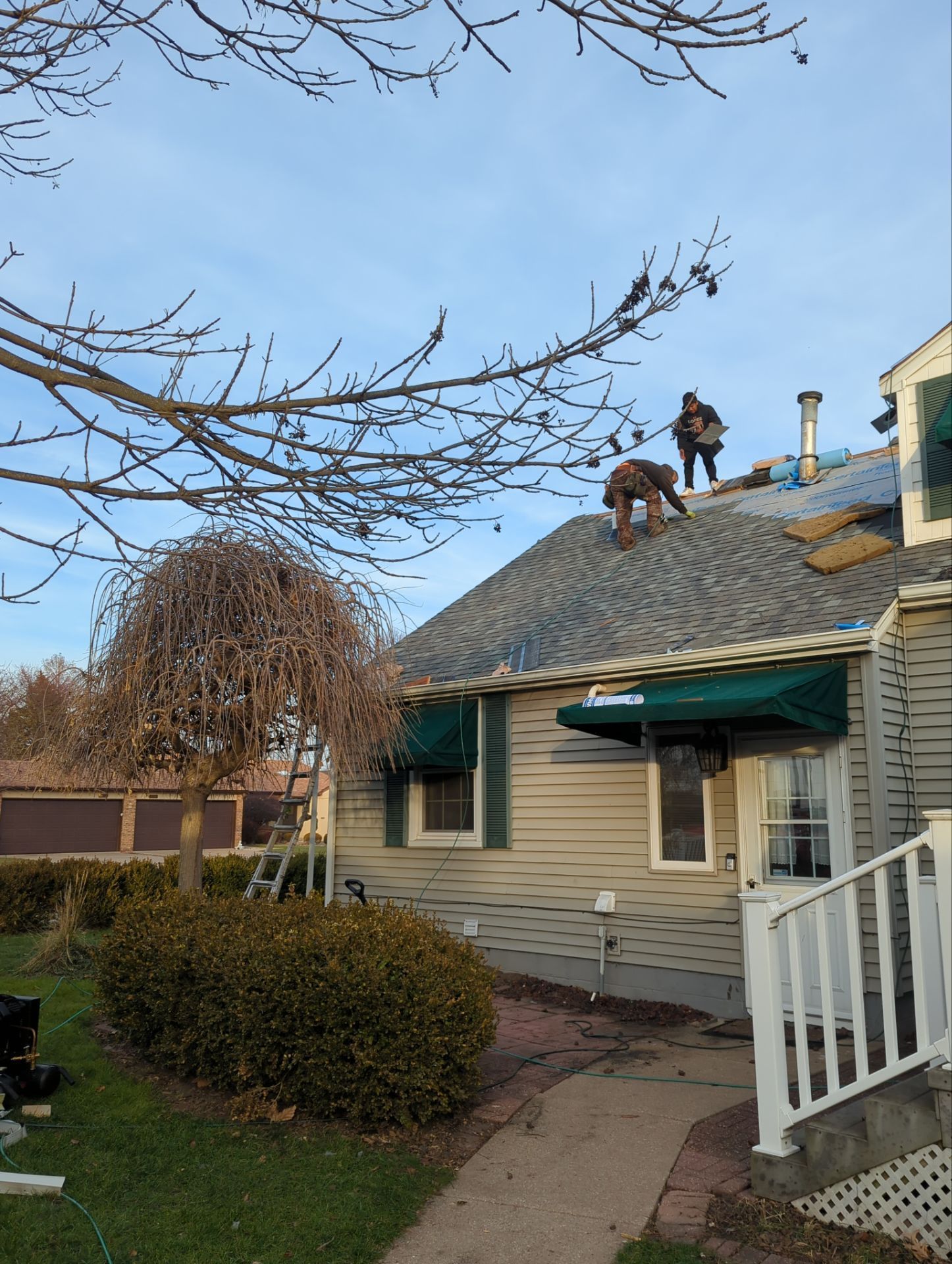 Workers repairing a house roof beside a front porch on a clear day