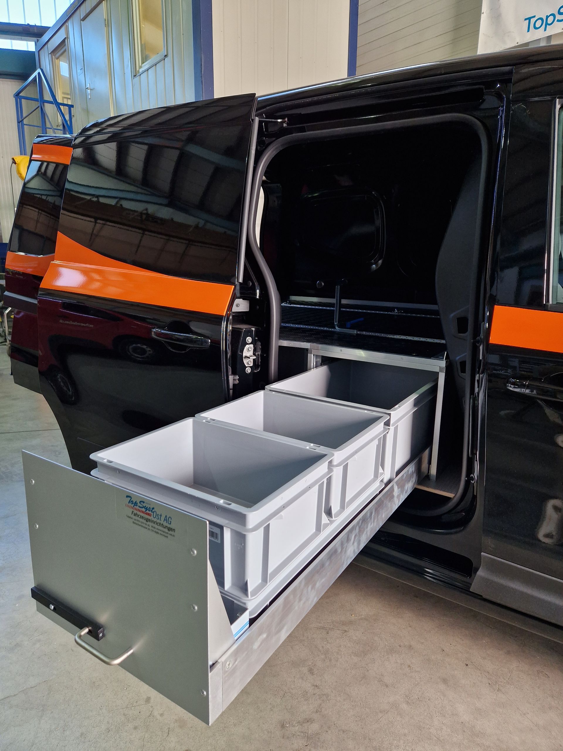 Schwarzer Lieferwagen mit offener Seitentür und einem ausziehbaren Schubladensystem mit drei grauen Aufbewahrungsbehältern.