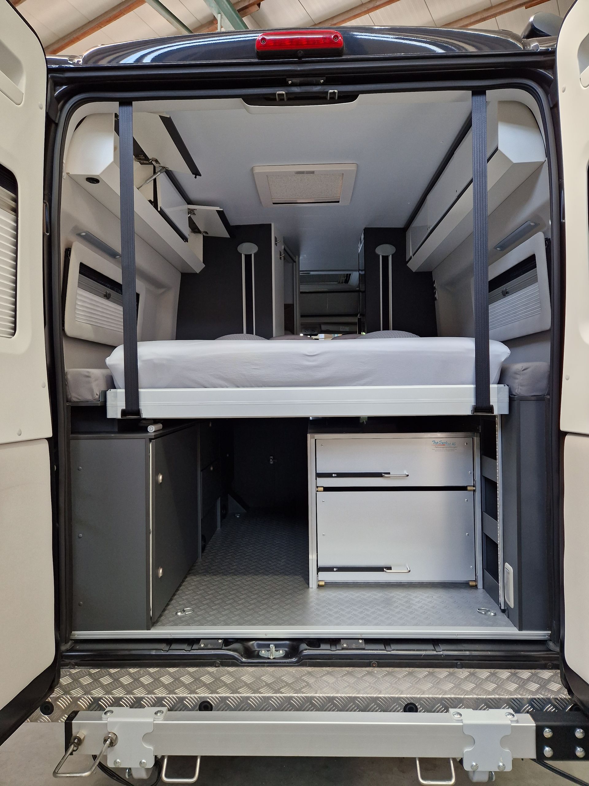 Innenraum eines Wohnmobils mit erhöhtem Bett, Stauraum und Metallboden.