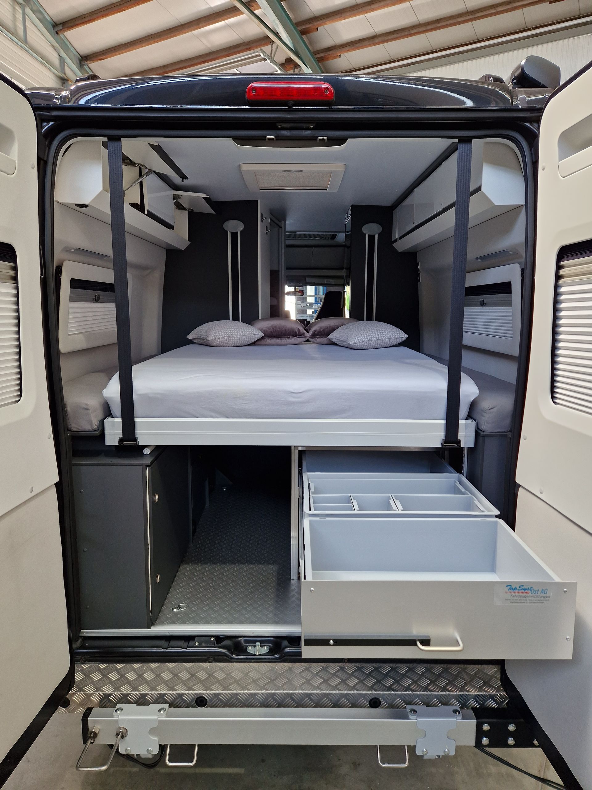 Innenansicht eines Wohnmobils mit hochgeklapptem Bett, geöffneten Schubladen und Stauschränken.