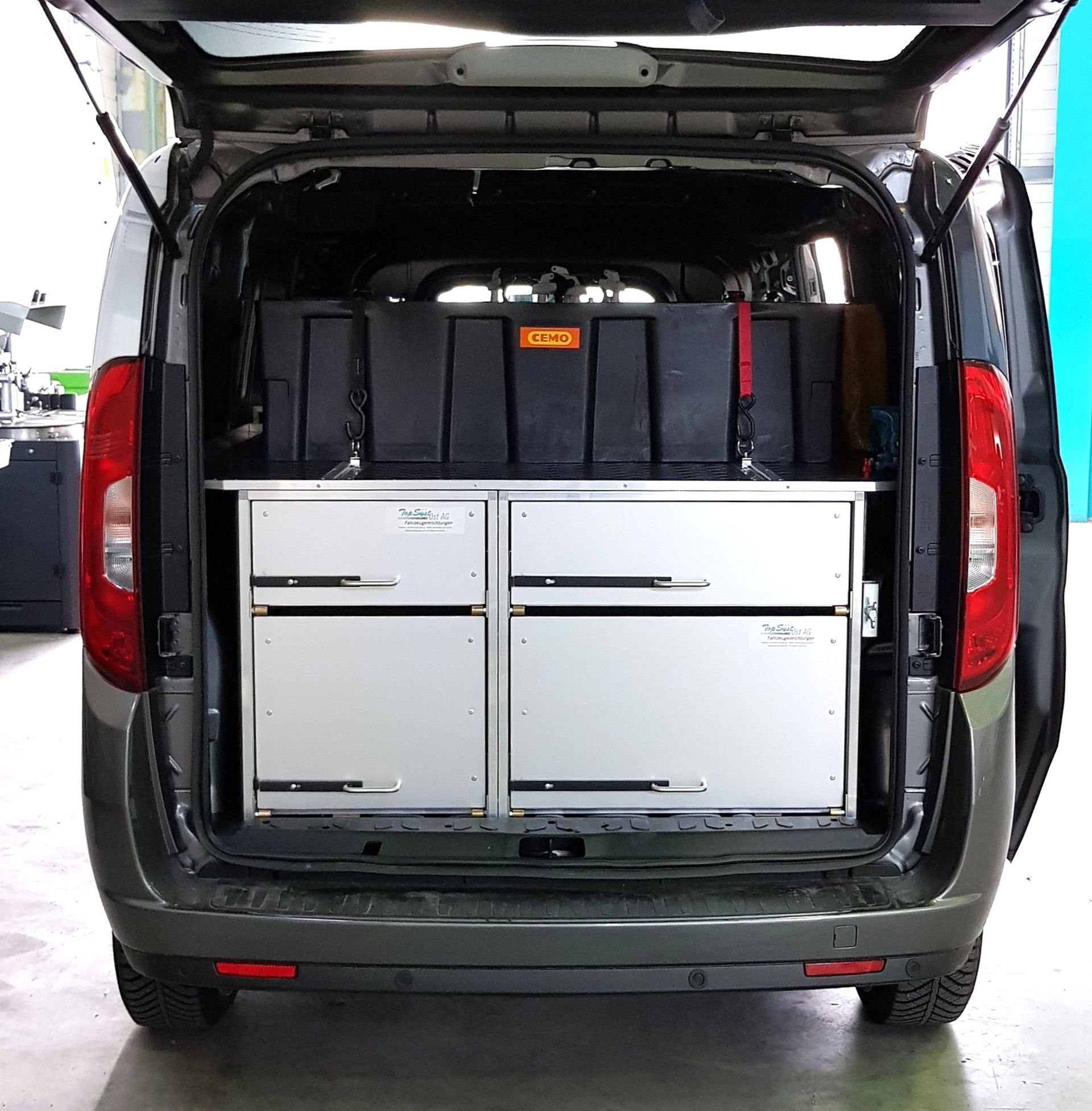 Van-Innenraum mit offenen Hecktüren, ausgestattet mit Aluminiumschubladen und schwarzen Aufbewahrungsbehältern.