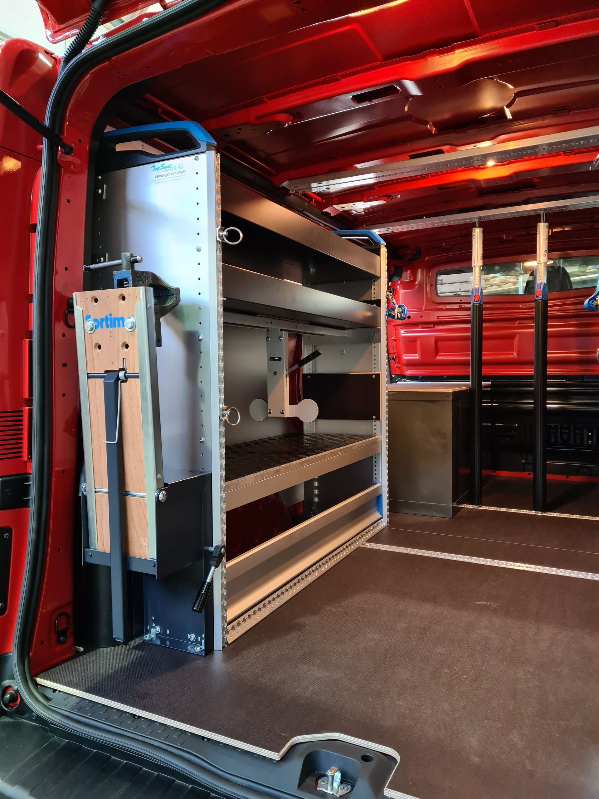 Roter Van-Innenraum mit Metallregal und heruntergeklappter Arbeitsfläche.