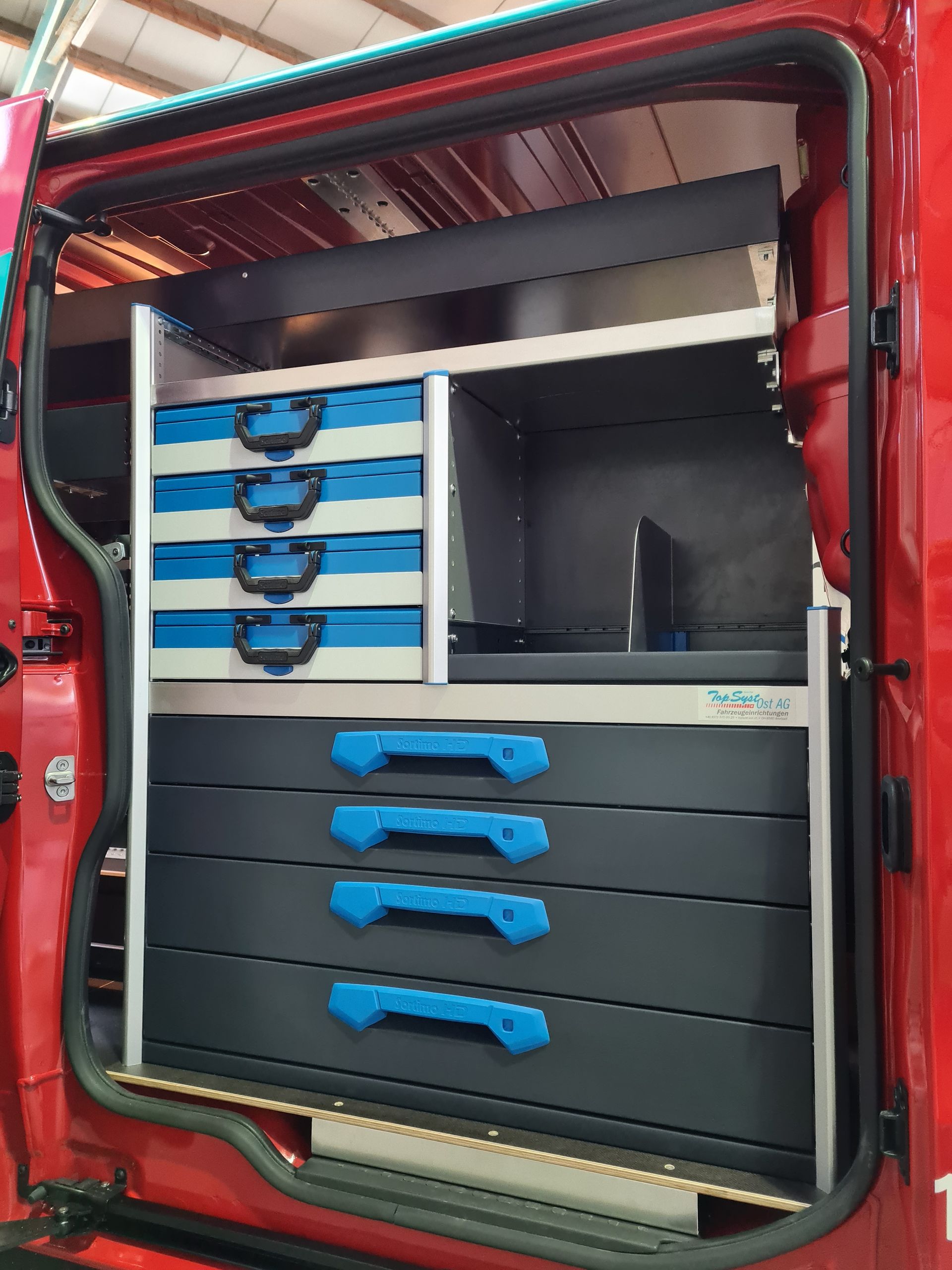 Roter Lieferwageninnenraum mit Regalen, Schubladen und Behältern mit blauen Griffen für Werkzeuge und Ausrüstung.