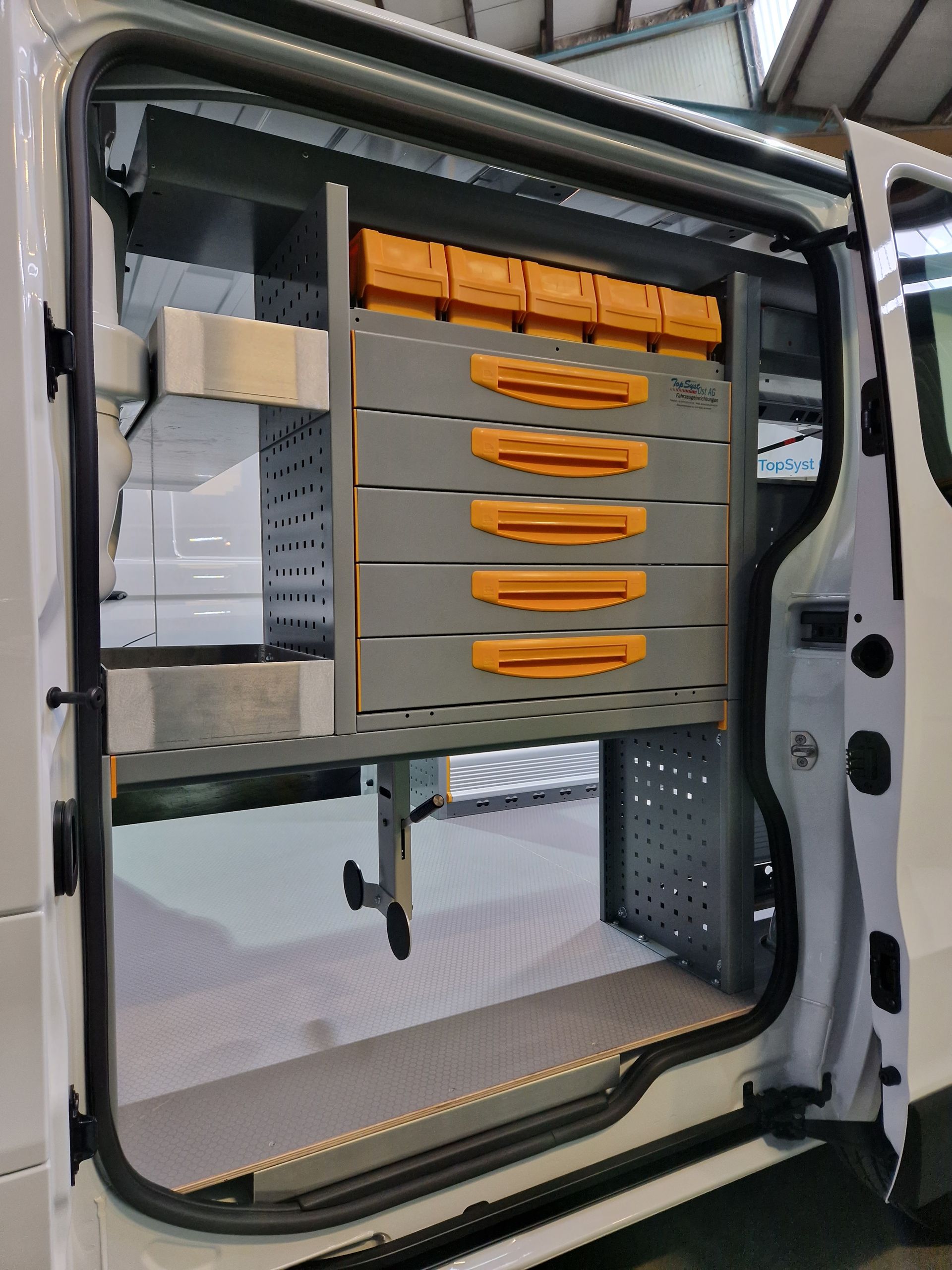 Weißer Van-Innenraum mit grauen Regalen, orangefarbenen Schubladen und Lagerbehältern.