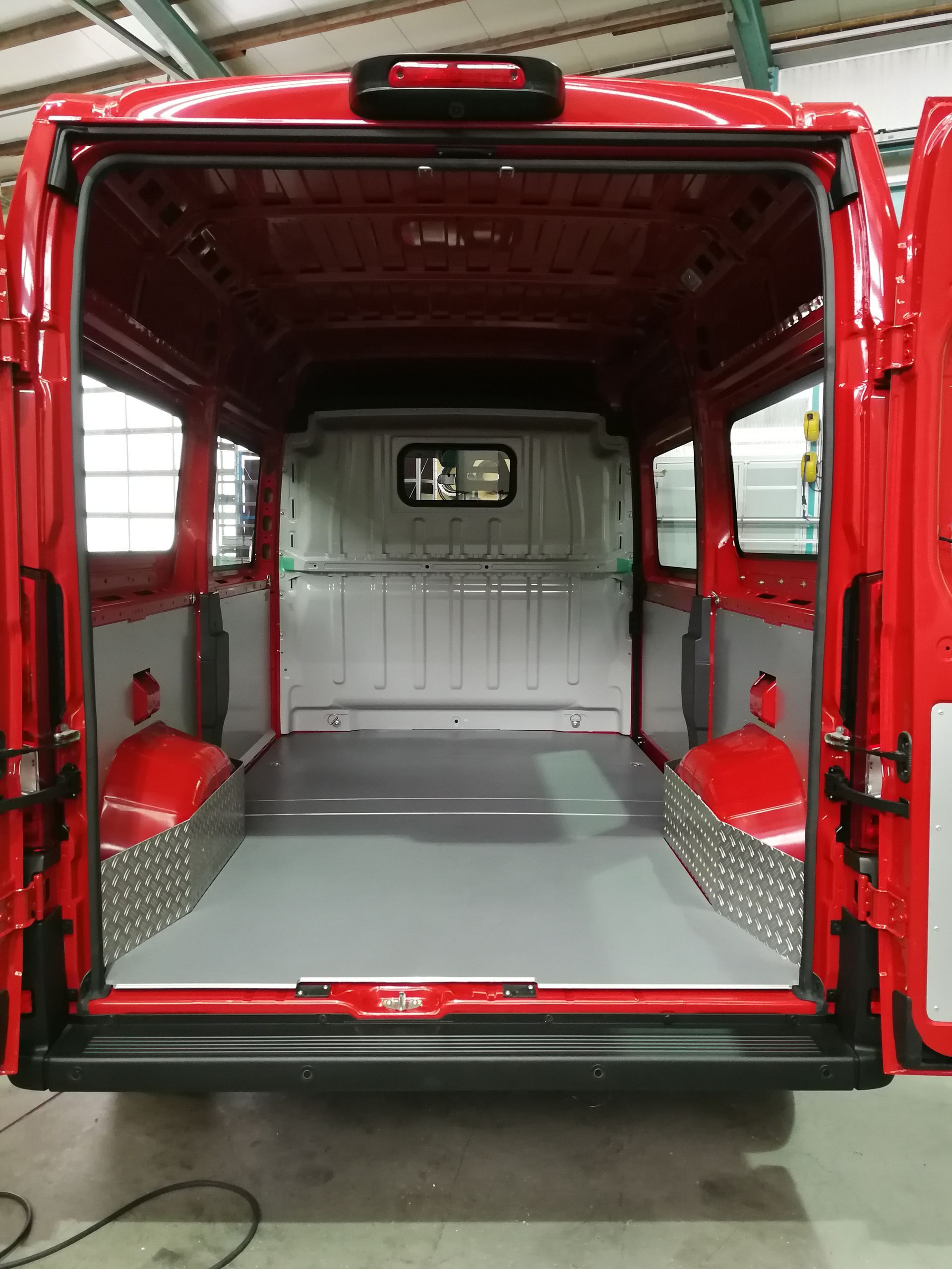 Innenraum eines roten Lieferwagens, leer, mit grauem Boden und Seitenwandschutz aus Metall.