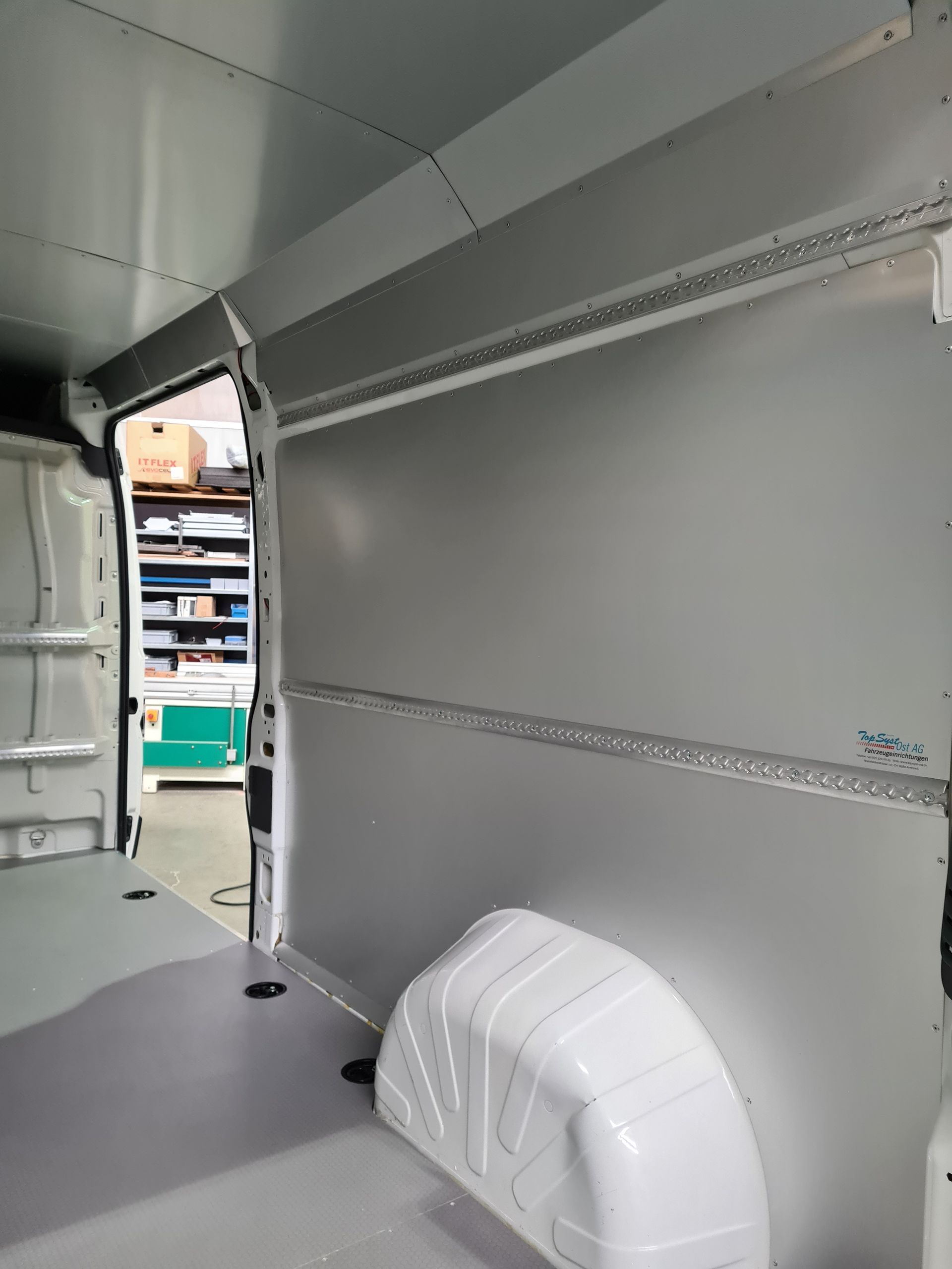 Innenraum eines weißen Lieferwagens mit grauer Verkleidung und Schienen zur Ladungssicherung.