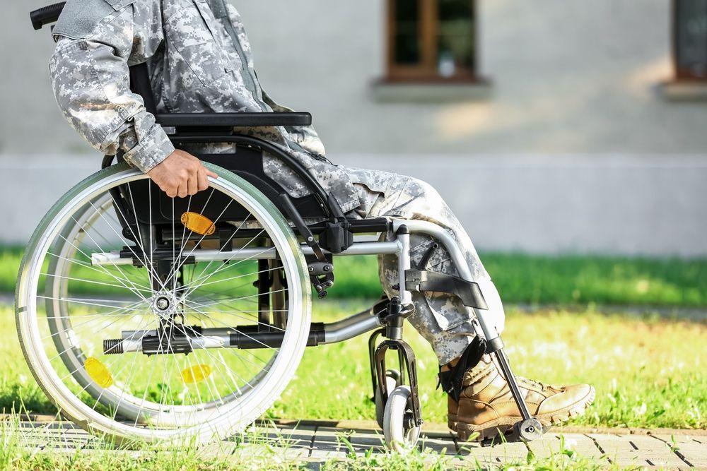 A soldier is sitting in a wheelchair on a sidewalk.