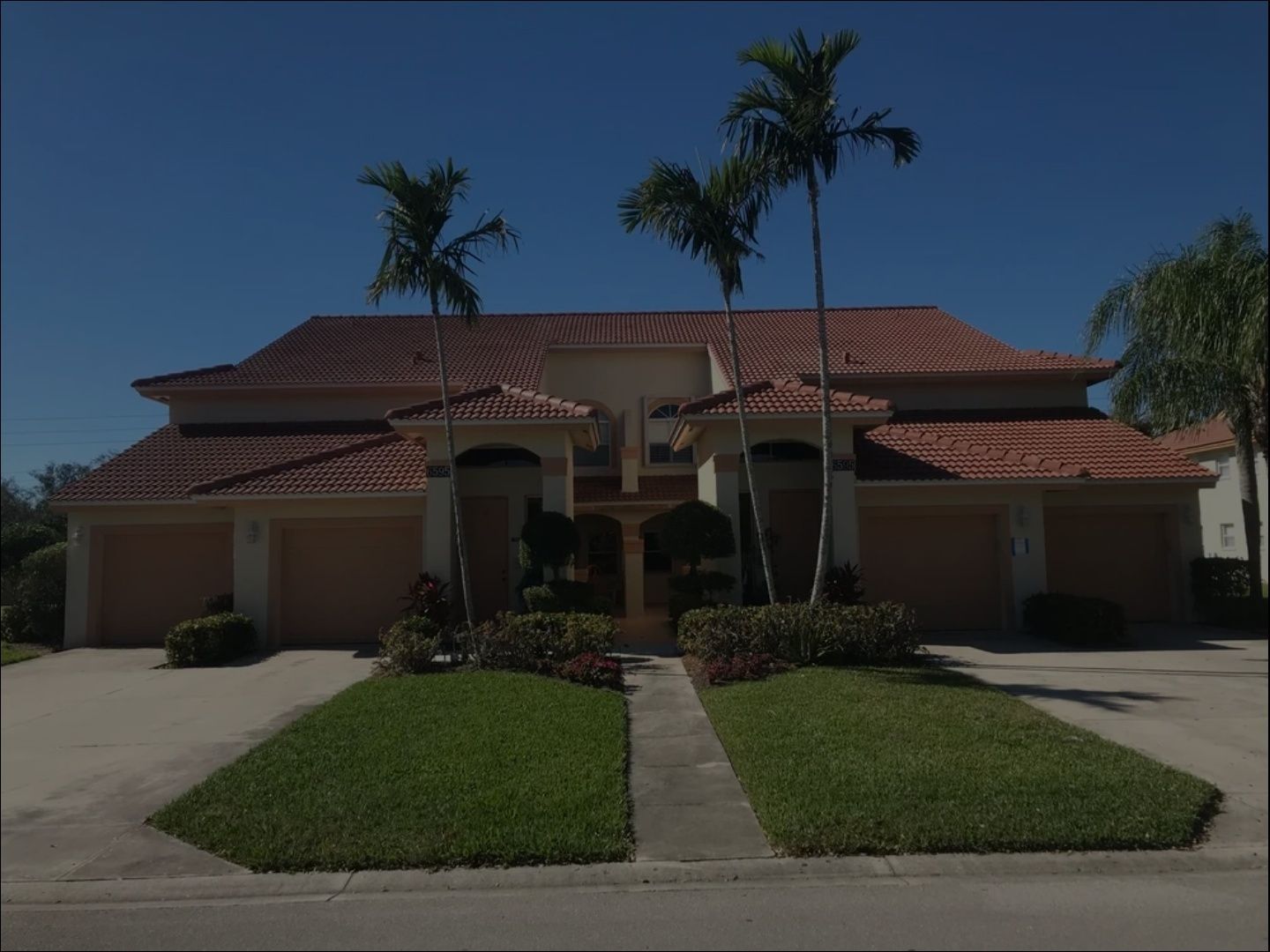 Large Mediterranean-style house with red-tile roof, palm trees, and two driveways under a clear blue sky