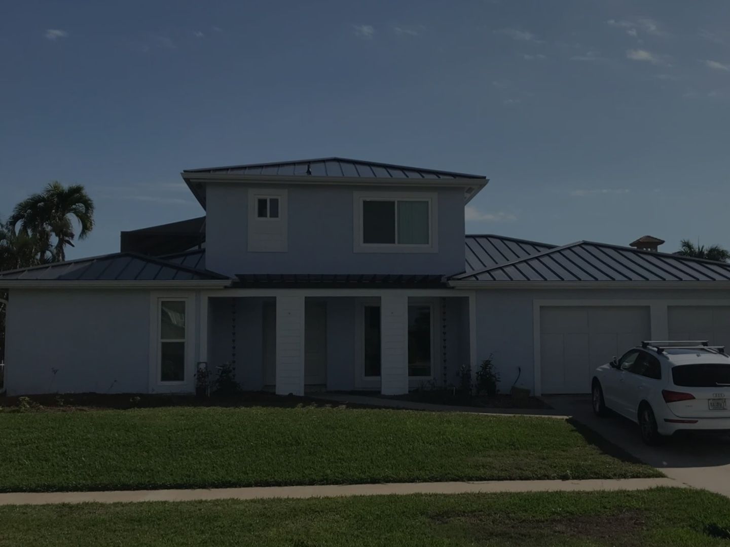 Two-story white house with a metal roof and front lawn, parked SUV on the right