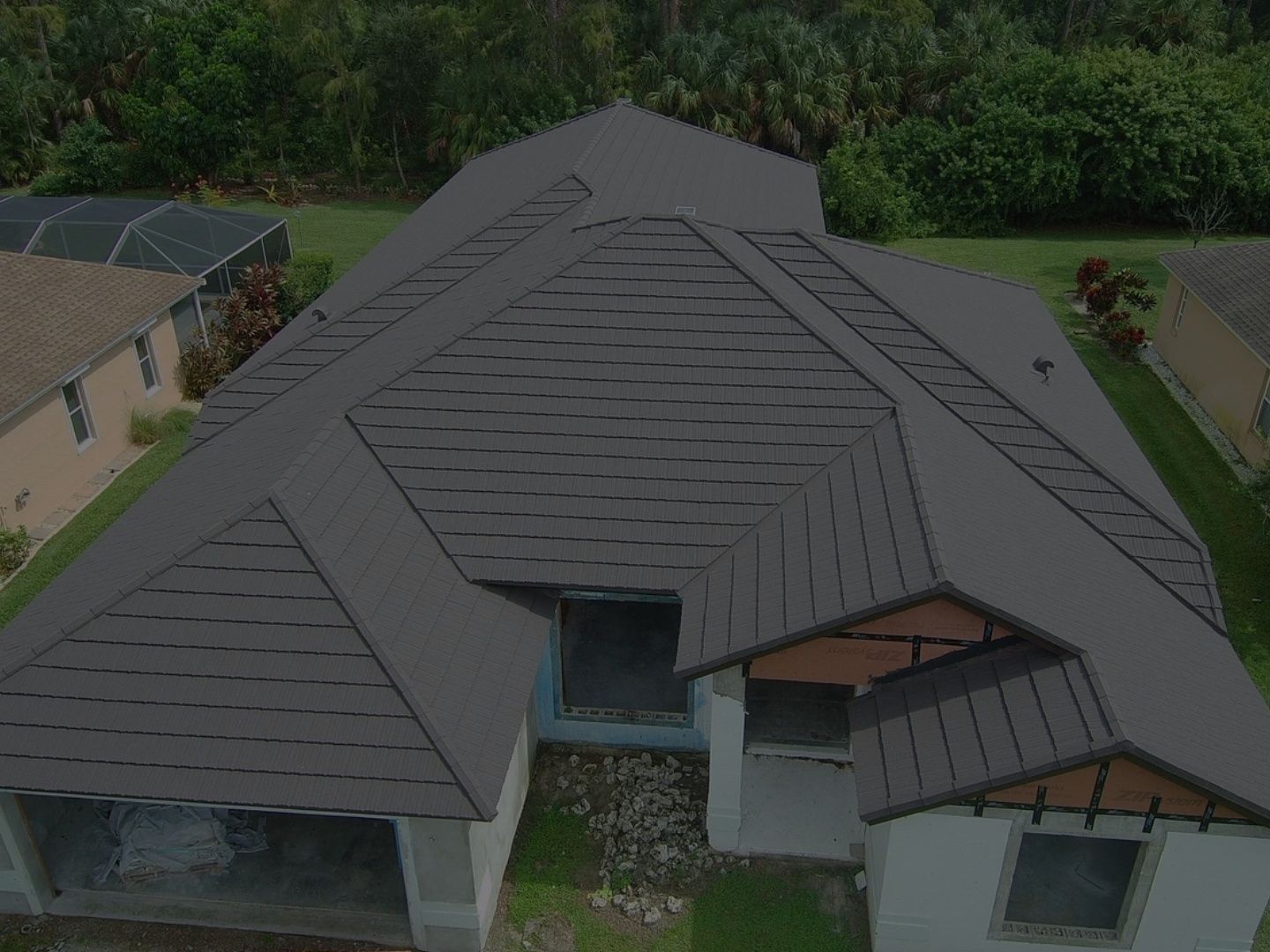 Aerial view of a modern building with a dark gray roof and surrounding greenery.