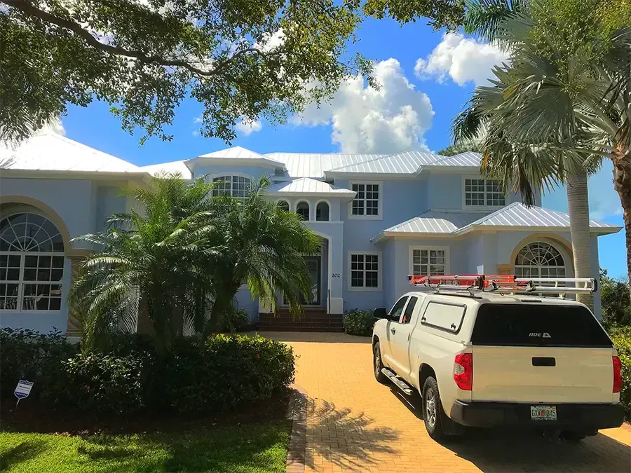 White house with palm trees and a pickup truck parked in a sunny driveway