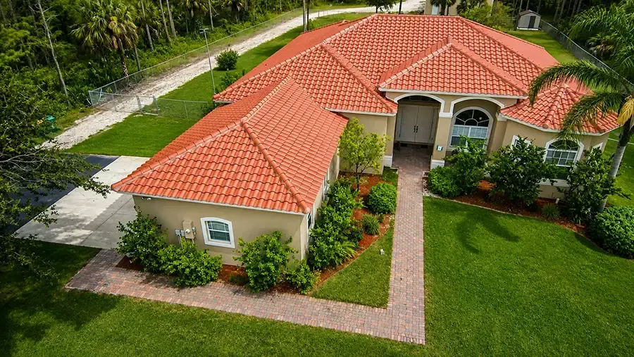 Aerial view of a beige house with a red tile roof, brick walkway, and lush green lawn.