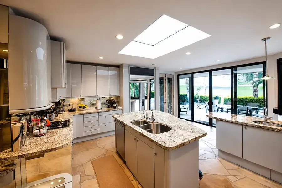 Bright modern kitchen with island, granite counters, skylights, and large glass doors to a patio
