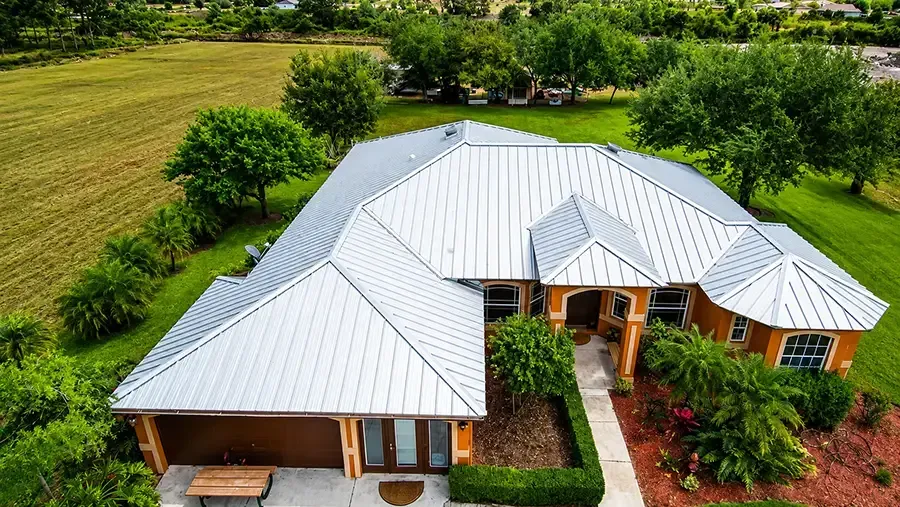 Aerial view of a white-roofed house with a wraparound porch surrounded by green fields and trees