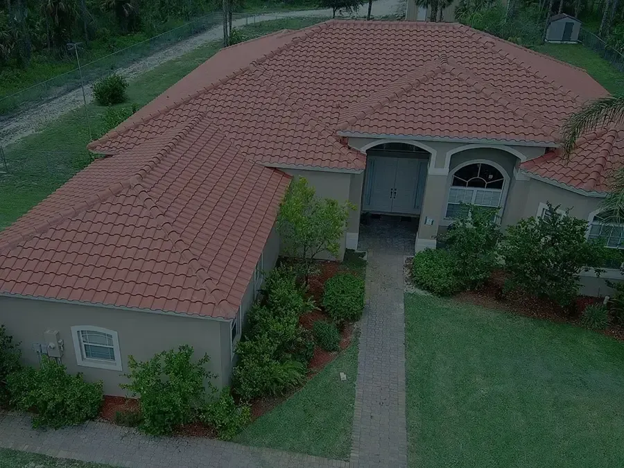 Aerial view of a single-story house with a red tile roof and front walkway surrounded by greenery