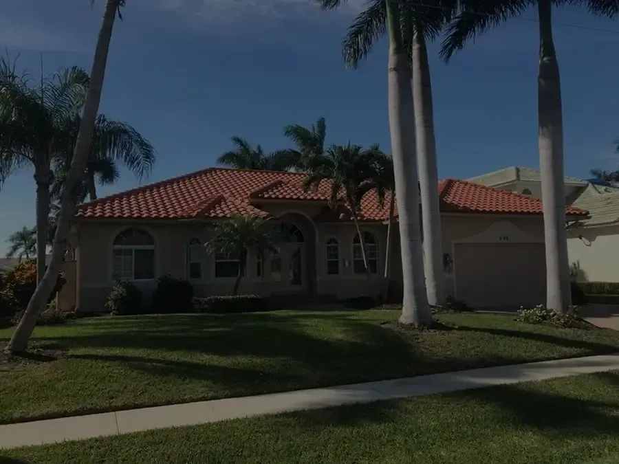 Single-story house with red tile roof, palm trees, and a manicured lawn in bright sunlight