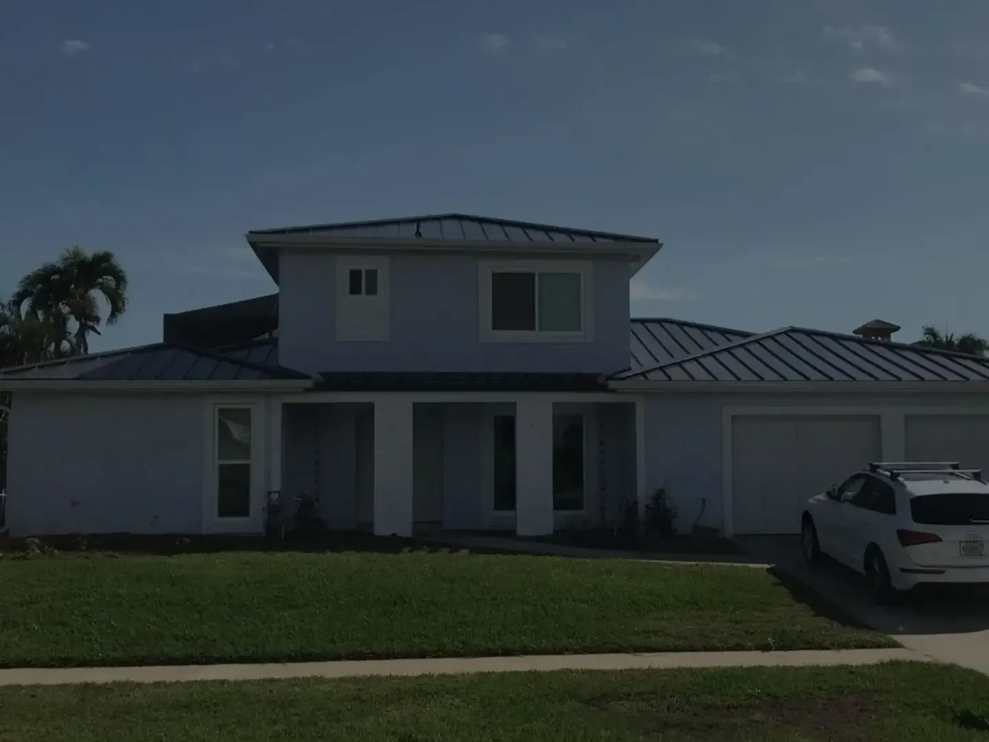 Modern two-story house with a metal roof, front lawn, and a white car parked in the driveway.