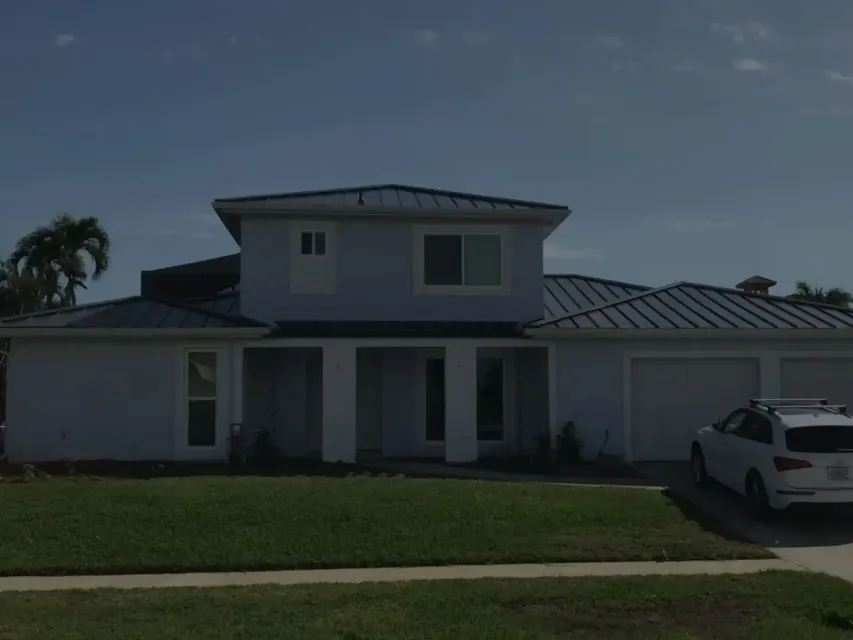 Two-story white house with a metal roof and front lawn, parked SUV on the right