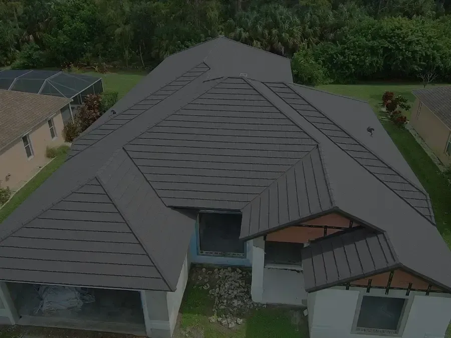 Aerial view of a large modern house with a dark gray roof and surrounding greenery.