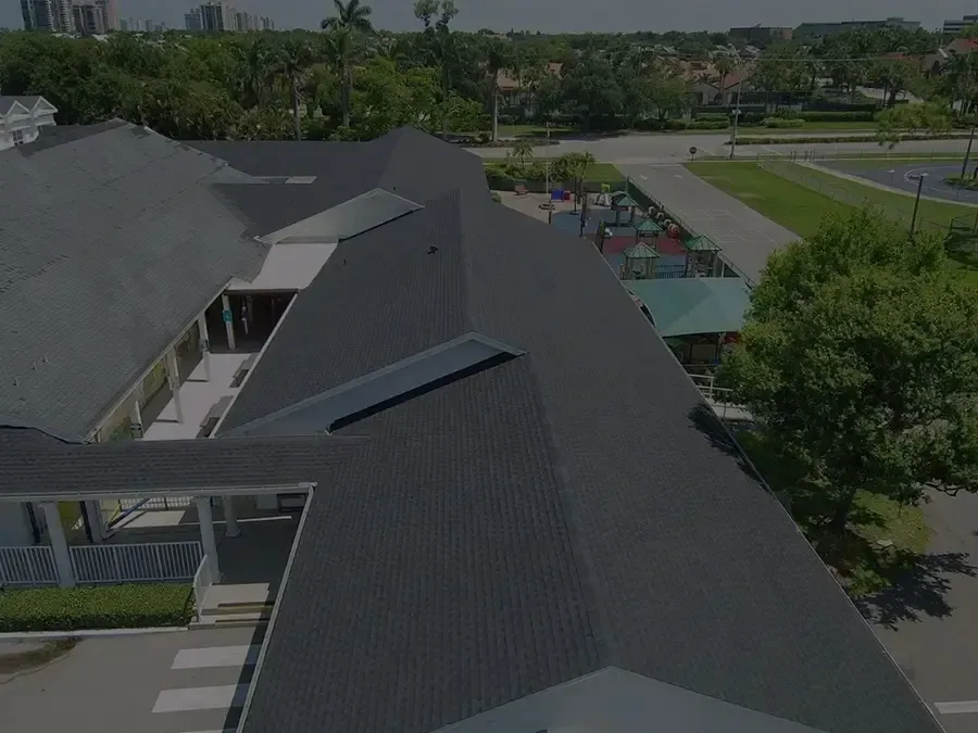 Aerial view of a modern building with dark roofs beside a park and road on a sunny day