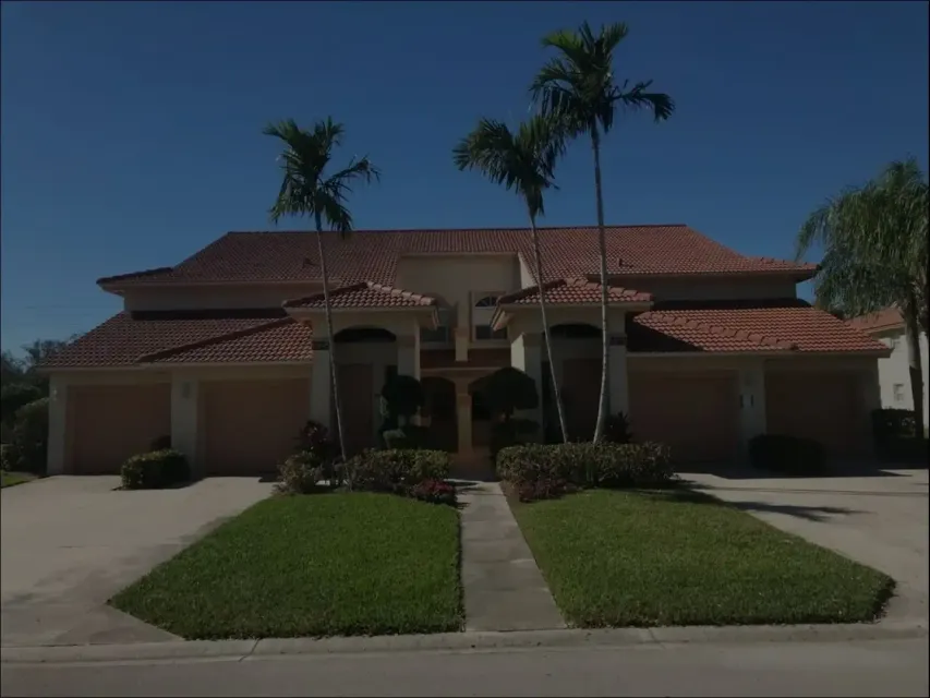 Large Mediterranean-style house with red-tile roof, palm trees, and two driveways under a clear blue sky