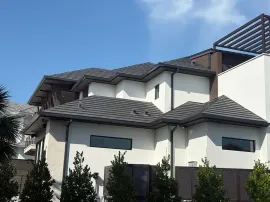Modern two-story house with gray tile roof and white stucco walls under a blue sky