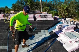 Worker in neon green shirt on a rooftop, handling materials beside stacks of insulation and tools.