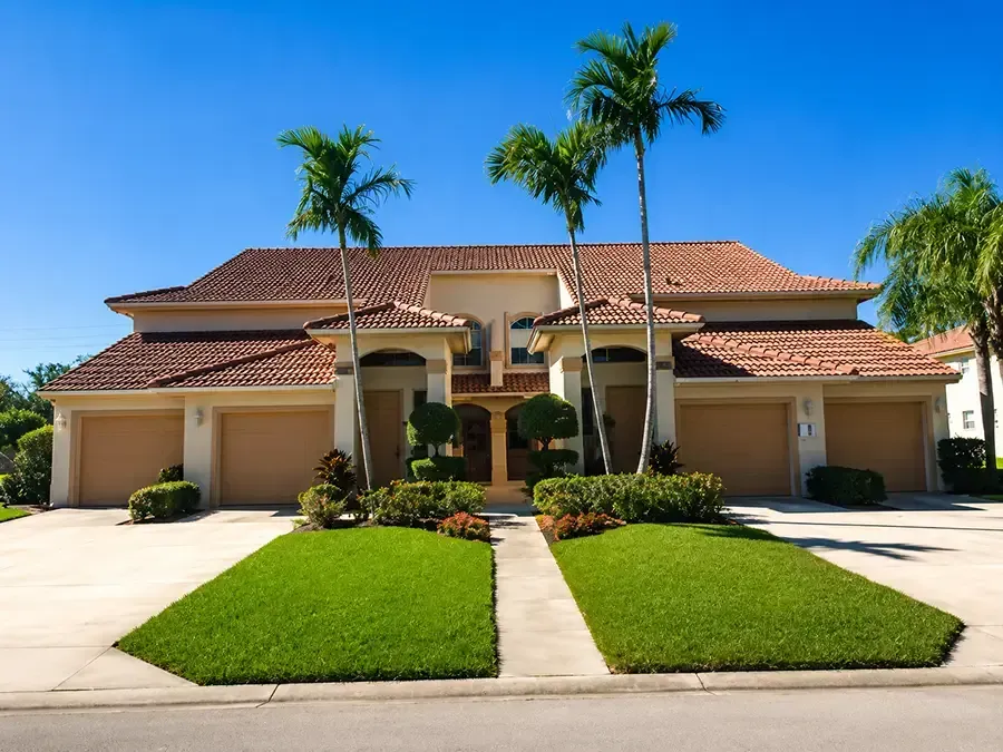 Two-story suburban homes with tiled roofs, palm trees, and manicured lawns under a clear blue sky