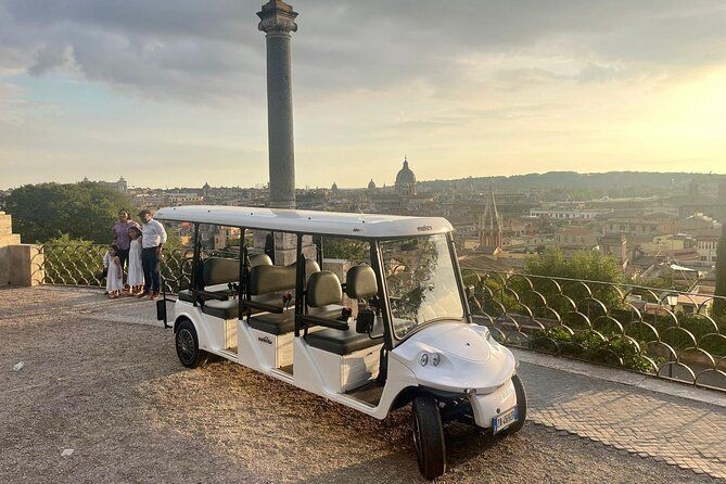 White golf cart parked at a scenic overlook with people and a city view at sunset