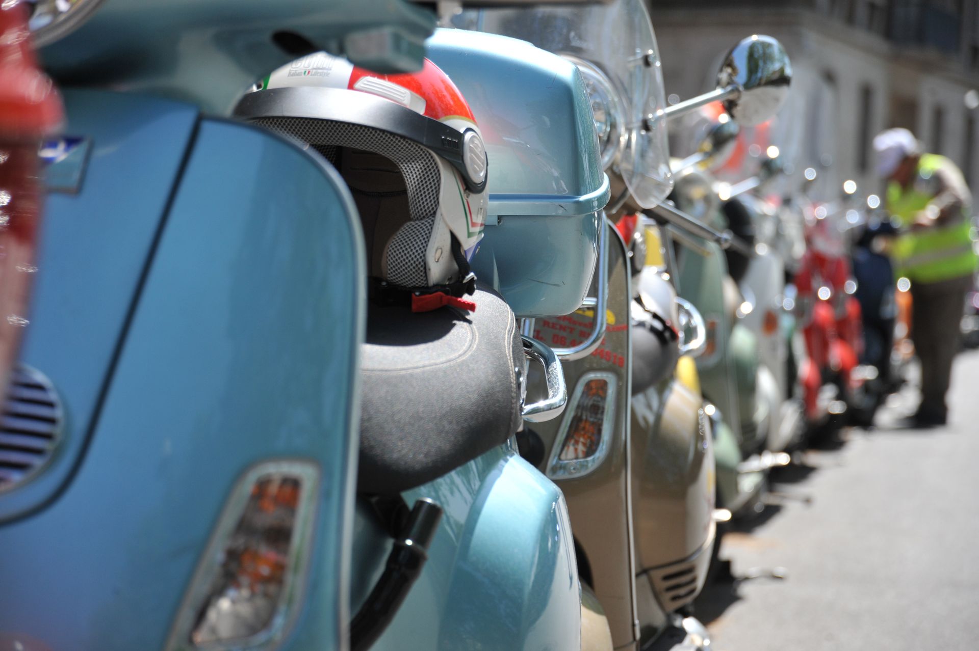 Row of parked scooters and motorcycles on a sunny street, with a blue scooter in the foreground