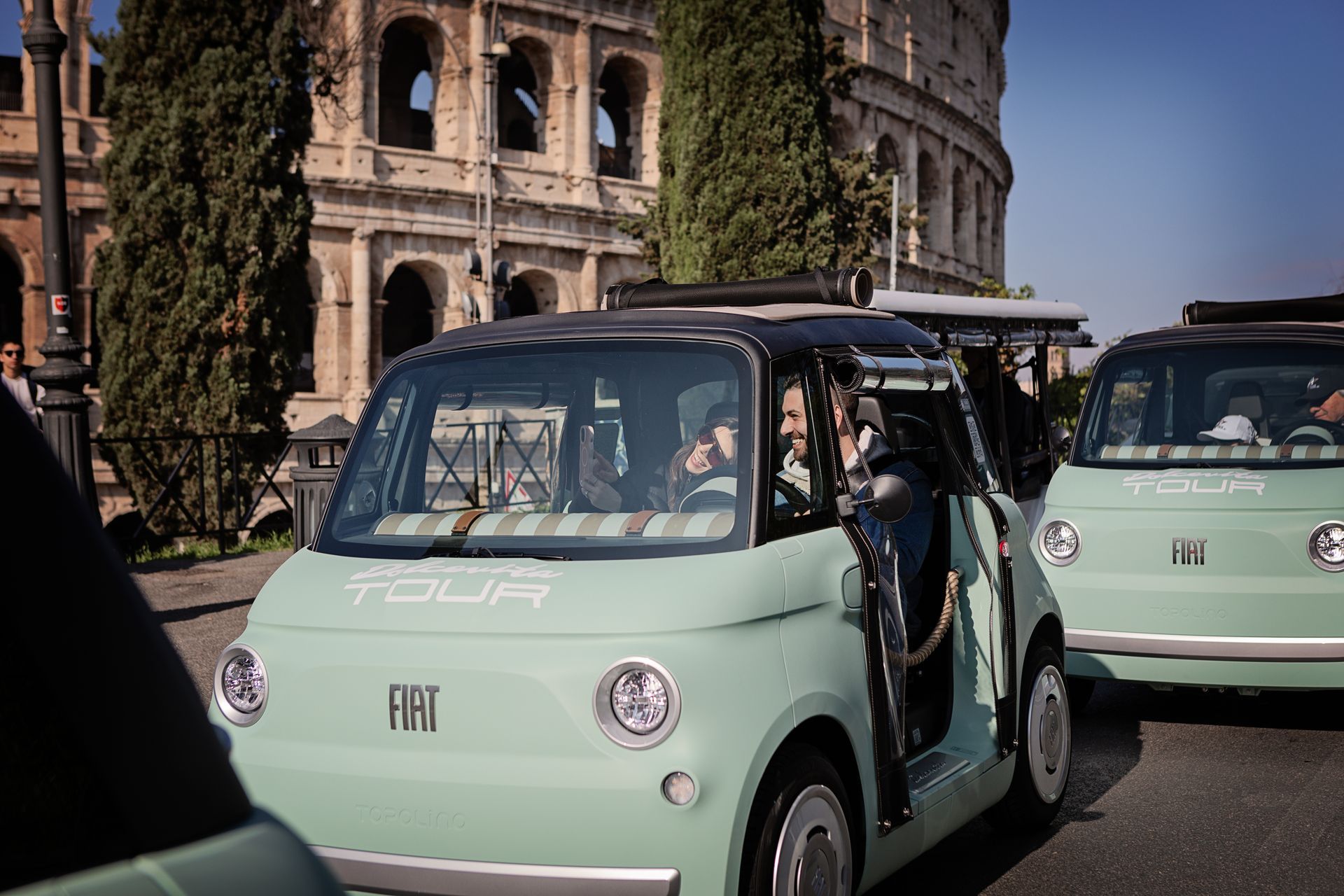 Mint-green electric microcars on a road beside the Colosseum in Rome