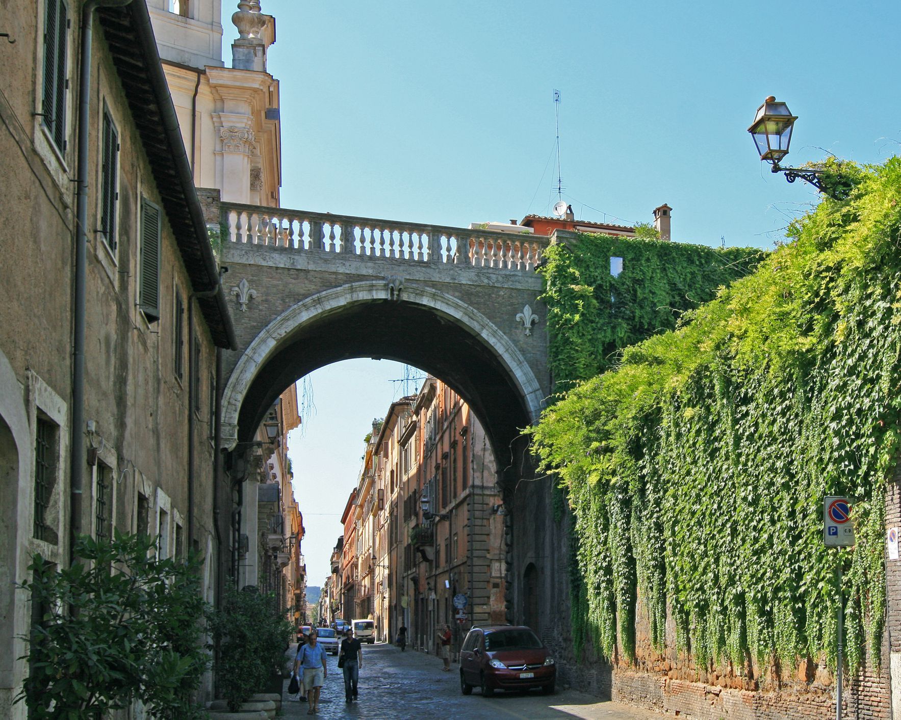 Narrow cobblestone street with stone buildings, ivy-covered wall, and an arched bridge overhead