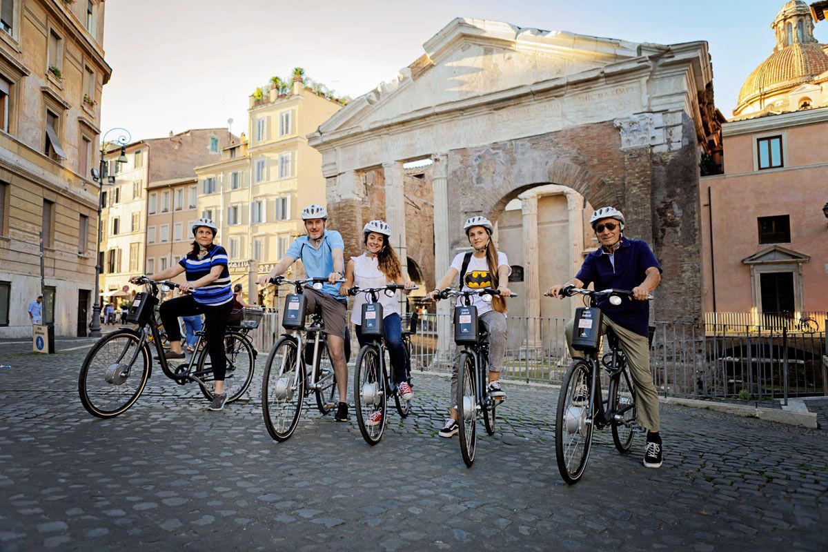 Group of cyclists riding on a cobblestone street in front of historic buildings.