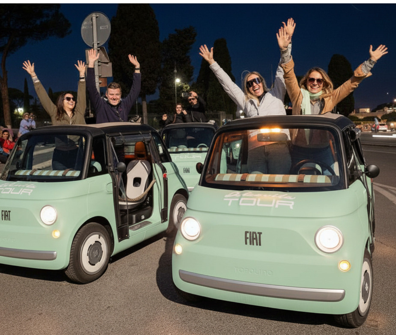 Two mint-green microcars at night with people riding inside, smiling and waving with raised arms.