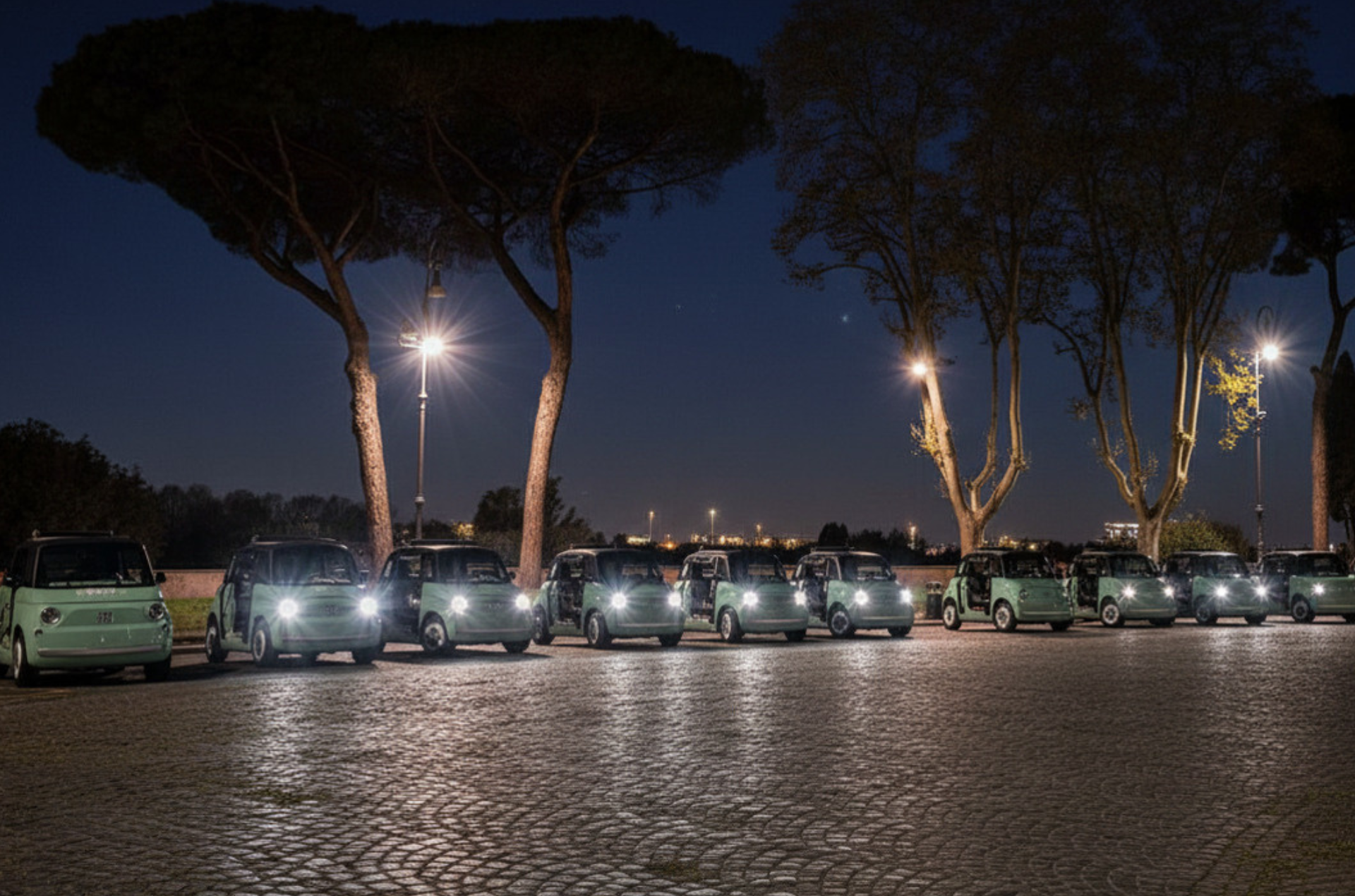 Row of parked SUVs at night under streetlights, seen across a cobblestone plaza.