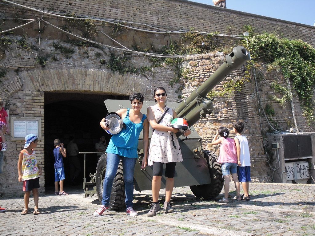 Visitors posing beside a large cannon at a stone fortress entrance