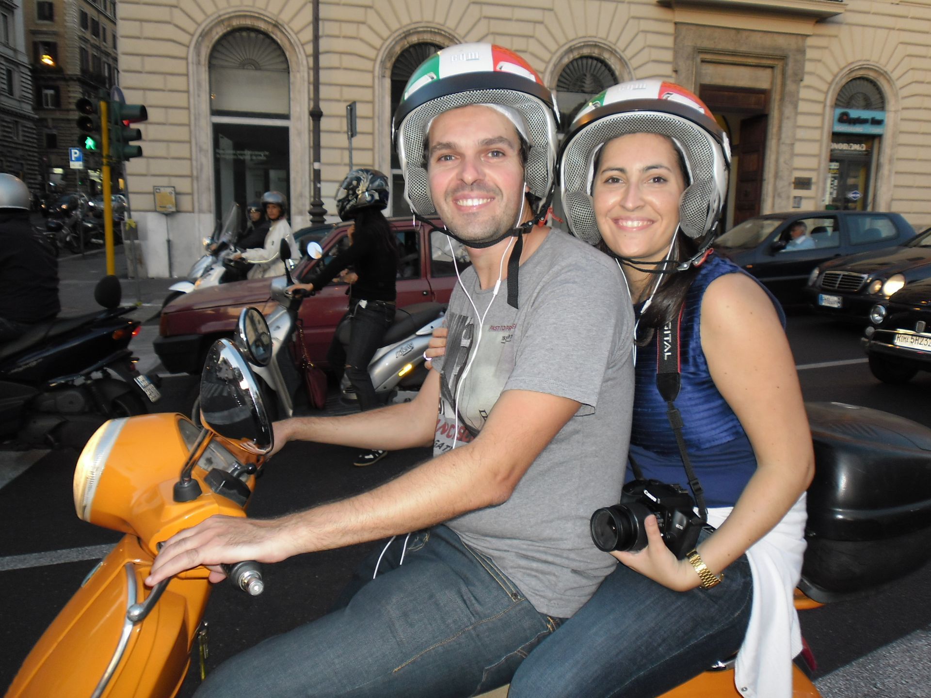Two people on an orange scooter wearing helmets, smiling on a city street at night