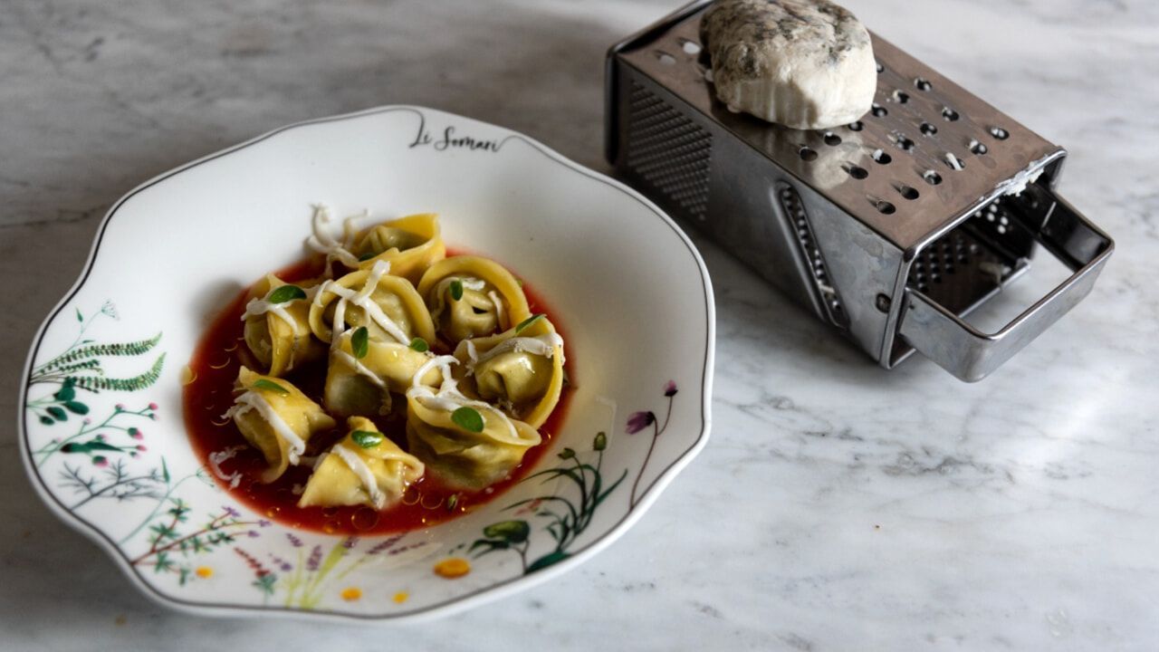 Plate of pasta with tomato sauce and shaved cheese beside a metal grater with cheese on a marble countertop