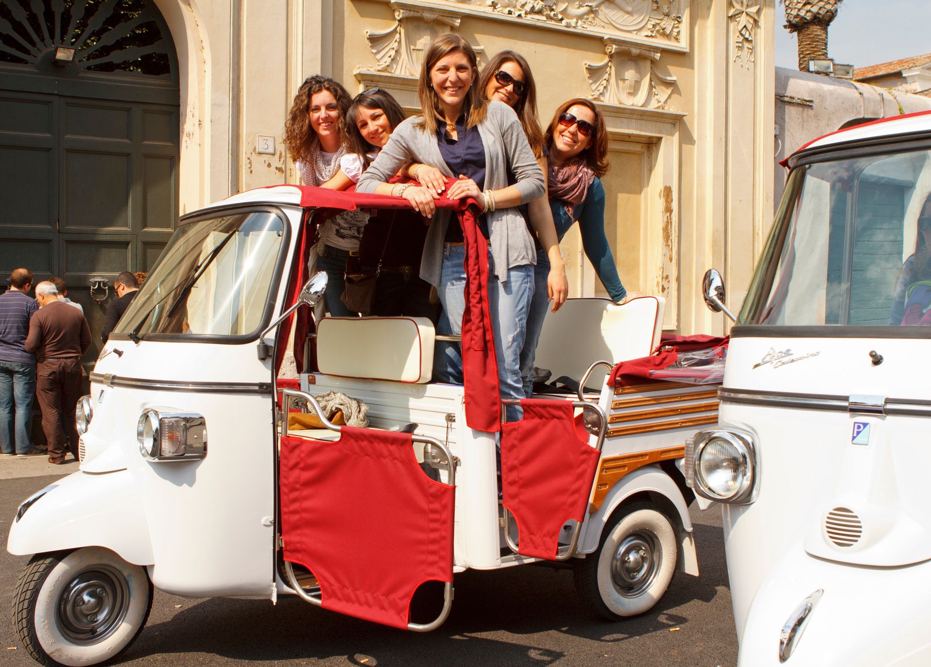 People posing on a red-and-white tuk-tuk in front of an ornate building
