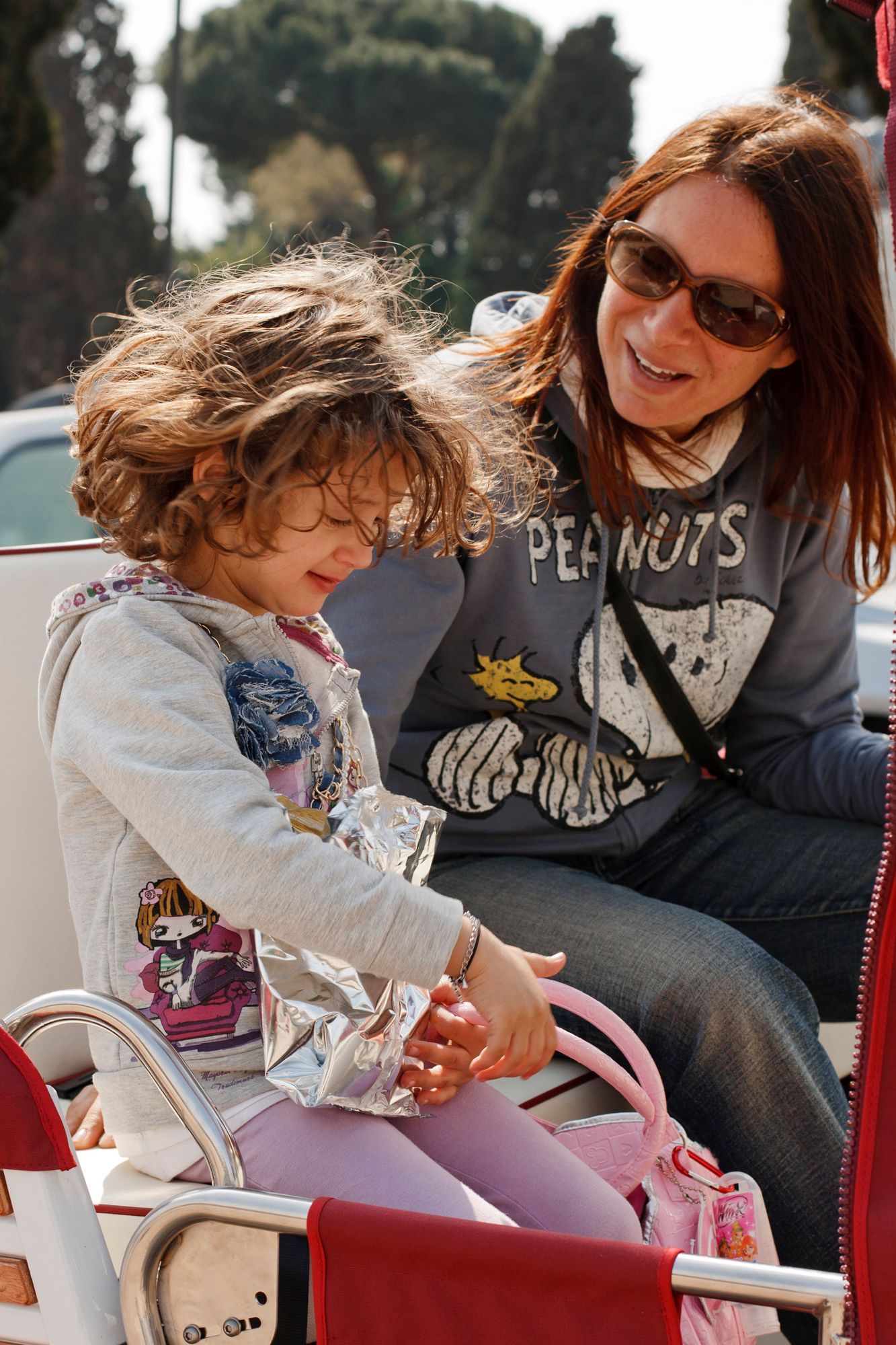 Woman and child sitting together outdoors, looking down at a pink stroller.