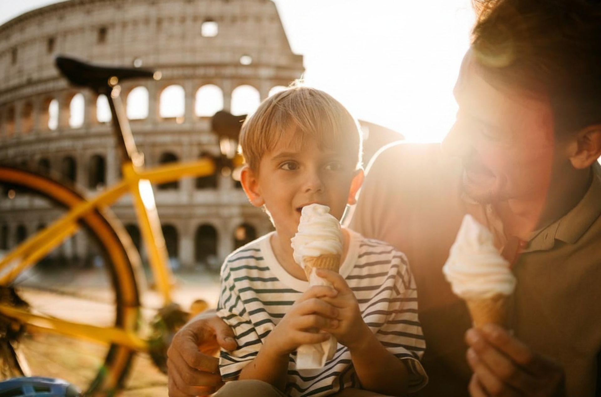 Child and adult sharing ice cream outdoors near the Colosseum with a bicycle in the foreground