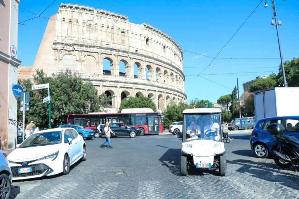Colosseum in Rome with cars and a small white vehicle on a sunny street