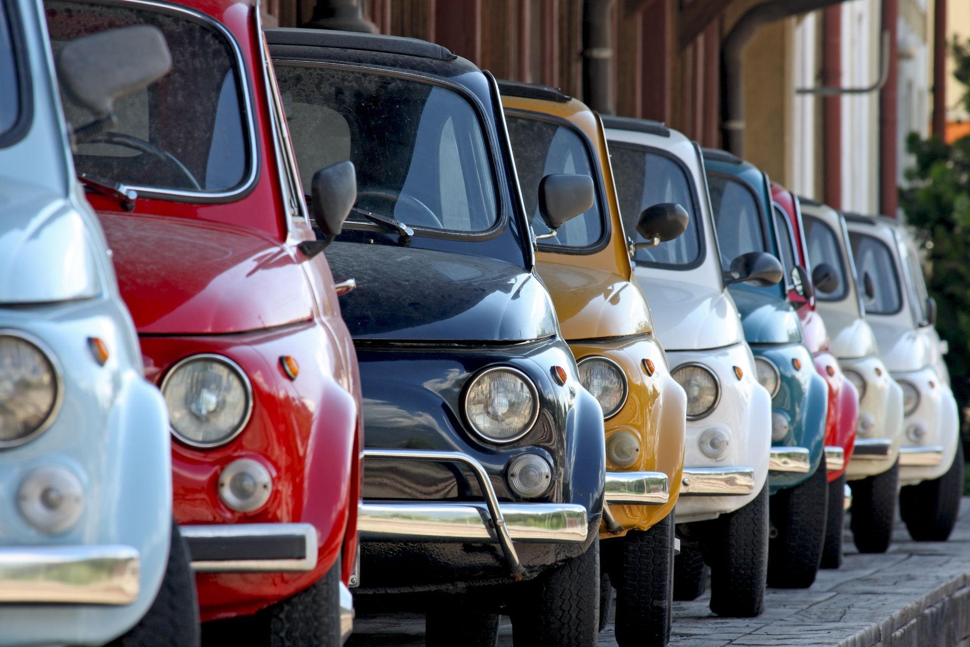 Row of colorful vintage cars parked along a street, viewed from the front-left