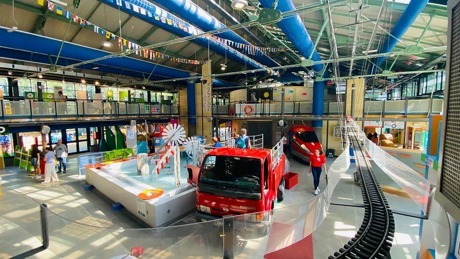 Indoor exhibition hall with two red fire trucks on display and visitors walking around