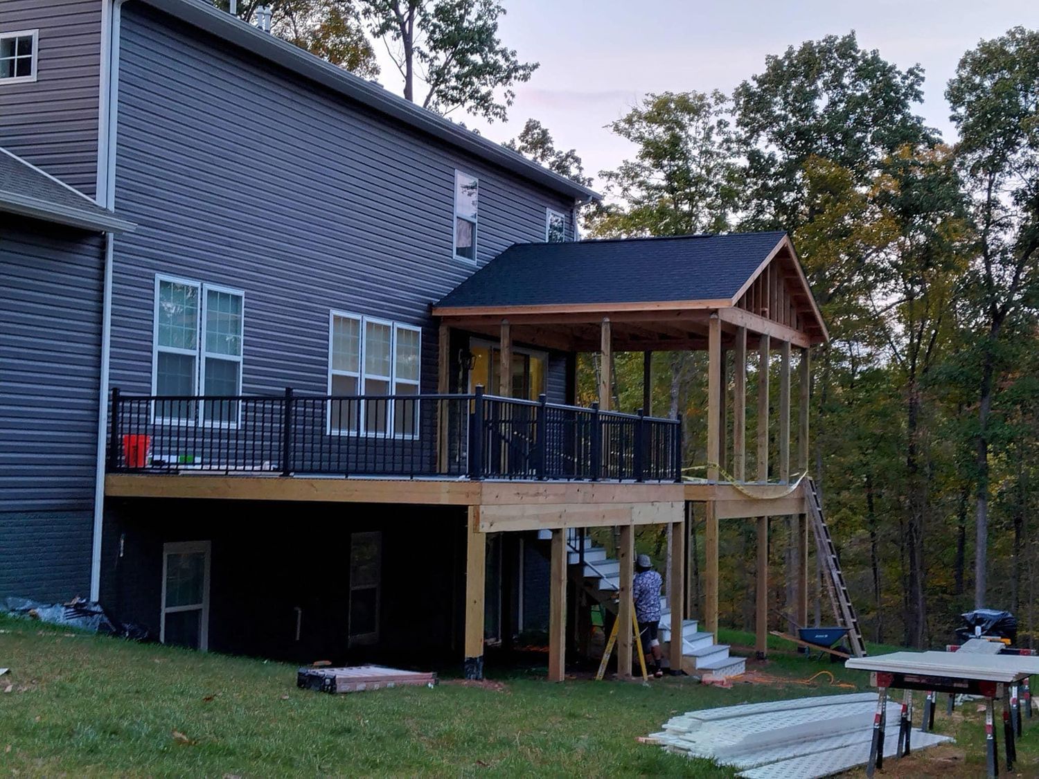 Back of house with deck and screened-in porch being built. Wood construction, gray siding, black railing, and a grassy yard.