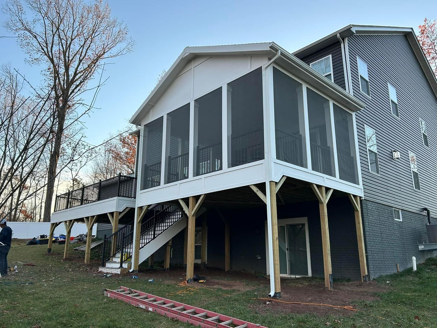 Screened porch addition on a two-story house, with stairs and an attached deck, viewed from a grassy yard.